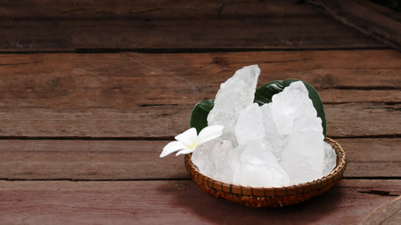 A basket filled with white alum crystals sits on a vibrant green shrub background. The contrasting colors highlight the purity of the alum against the lush greenery, creating fresh feeling.の写真素材