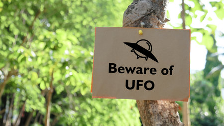Illustrated with a black UFO space ship the paper sign prominently displays the words Beware of UFO. Warning everyone to the potential danger of aliens.の写真素材