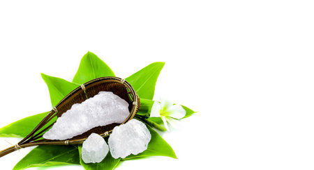 White crystal clear alum cube on green leaf isolated on white background. The chemical compound substance concept of spa and beauty industry.の写真素材