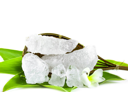 White crystal clear alum cube on green leaf isolated on white background. The chemical compound substance concept of spa and beauty industry.の写真素材