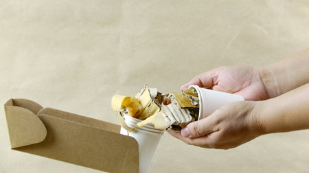 Hands holding a white paper coffee cup and used paper on a brown surface, awaiting recycling. Promotes recycling waste, saving the Earth, and conserving natural resources.の写真素材