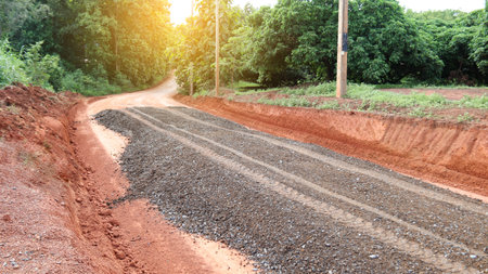 Image of gravels being leveled on a dirt road in preparation for asphalt paving for new road construction. Perfect for illustrating road-building processes.の写真素材