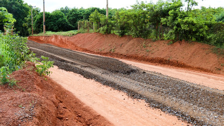 Image of gravels being leveled on a dirt road in preparation for asphalt paving for new road construction. Perfect for illustrating road-building processes.の写真素材