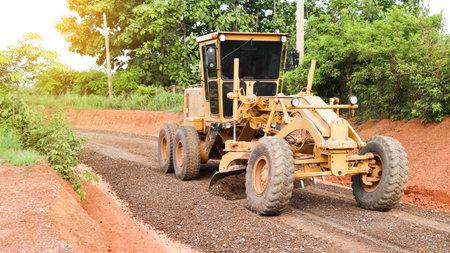Image of a grader leveling gravels on a dirt road in preparation for asphalt paving for new road construction. Perfect for illustrating road-building processes.の写真素材