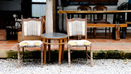 Two old, wooden chairs and rock top table placed in front of a cozy coffee shop, inviting passersby to sit and enjoy a moment of relaxation.の写真素材
