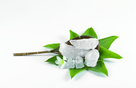 Clear and pristine alum cubes resting in a bamboo basket alongside leaves, set against a white background, showcasing the natural purity and traditional presentation of the substance.の写真素材