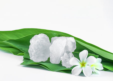 Clear and pristine alum cubes resting in a bamboo basket alongside leaves, set against a white background, showcasing the natural purity and traditional presentation of the substance.の写真素材