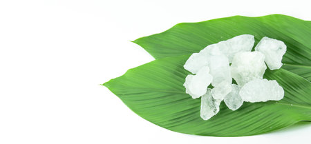Clear and pristine alum cubes resting in a bamboo basket alongside leaves, set against a white background, showcasing the natural purity and traditional presentation of the substance.の写真素材