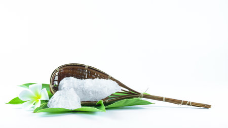 Clear and pristine alum cubes resting in a bamboo basket alongside leaves, set against a white background, showcasing the natural purity and traditional presentation of the substance.の写真素材