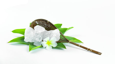 Clear and pristine alum cubes resting in a bamboo basket alongside leaves, set against a white background, showcasing the natural purity and traditional presentation of the substance.の写真素材