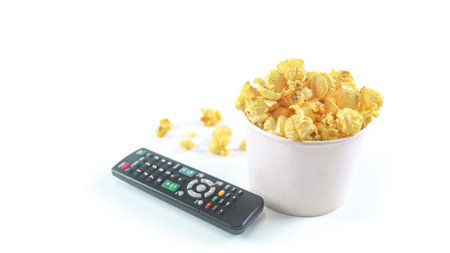 Isolated image of popcorn in paper cup and TV remote control set against a white background, showcasing the fluffy, perfect for themes related to snacks, cinema, or casual dining.の写真素材