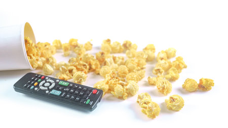 Isolated image of popcorn in paper cup and TV remote control set against a white background, showcasing the fluffy, perfect for themes related to snacks, cinema, or casual dining.の写真素材