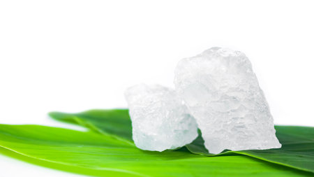 White crystal clear alum cube on green leaf isolated on white background. The chemical compound substance concept of spa and beauty industry.の写真素材