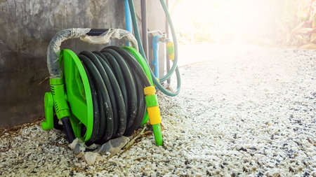 A garden hose coiled neatly in its holder, resting on a stone paved yard. The scene evokes a peaceful, well maintained garden space, with the hose ready for use.の写真素材