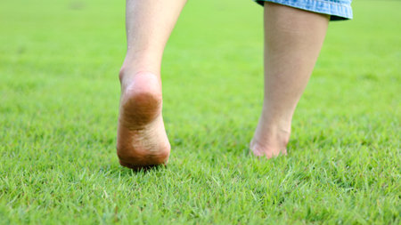 Bare feet walking on grass ground, symbolizing the idea of healing, promoting both physical and mental well being through grounding and connection with nature.の写真素材
