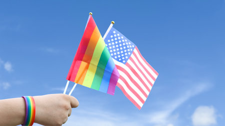 Cut out of hand holding both the LGBT flag and the American flag, set against blue sky background with clipping paths. The symbolizing unity, diversity, and inclusion.の写真素材
