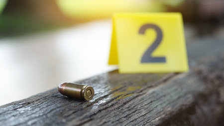 9 mm pistol copper head bullet lying on dark wooden bench with blur number 2 sign on blur background. Concepts of criminal investigations and shooting sport.の写真素材