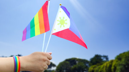 Cut out of hand holding both the LGBT flag and the Philippines flag, set against blue sky background with clipping paths. The symbolizing unity, diversity, and inclusion.の写真素材