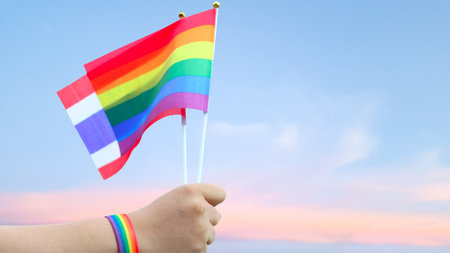 Cut out of hand holding both the LGBT flag and Thailand flag, set against blue sky background with clipping paths. The symbolizing unity, diversity, and inclusion.の写真素材