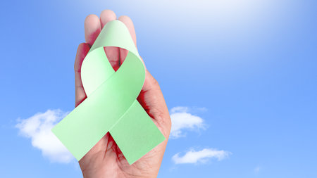 Hand holding green ribbon, symbolizing ovarain cancer awareness. Ribbon represents hope and unity, raising awareness and support for those affected by cancer, fostering understanding and prevention.の写真素材