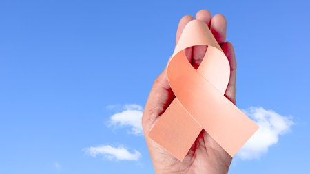 Hand holding peach ribbon, symbolizing uterine cancer awareness. Enhance hope and unity, raising awareness and support for those affected by cancer, fostering understanding and prevention.の写真素材