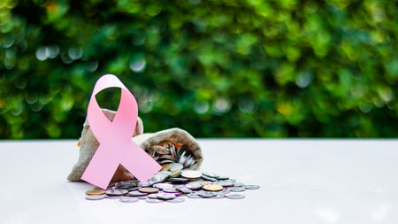 Pink ribbon, symbolizing cancer awareness, placed on a burlap sack filled with coins, representing raising awareness and supporting cancer related causes through donation fundsの写真素材