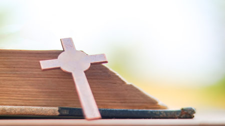 Dark red copper cross leaning against an old open book symbolizing the spread of Jesus Christs love among Christians reflecting faith devotion and the importance of Christian teachings.の写真素材