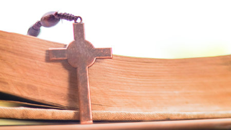 Dark red copper cross leaning against an old open book symbolizing the spread of Jesus Christs love...
