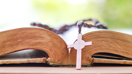 Dark red copper cross leaning against an old open book symbolizing the spread of Jesus Christs love among Christians reflecting faith devotion and the importance of Christian teachings.の写真素材