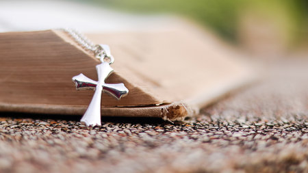 Shiny metal cross leaning against an old open book symbolizing the spread of Jesus Christs love...