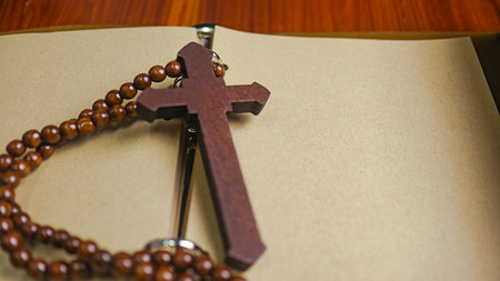 Dark red wooden cross leaning against an old open book symbolizing the spread of Jesus Christs love...