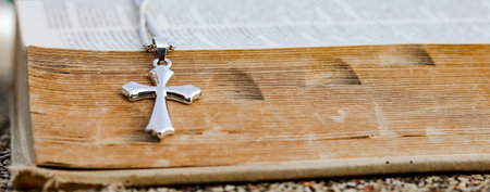 Shiny metal cross leaning against an old open book symbolizing the spread of Jesus Christs love among Christians reflecting faith devotion and the importance of Christian teachings.の写真素材