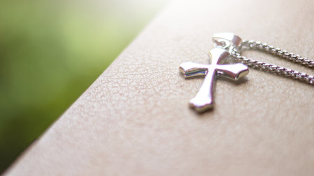 Shiny metal cross leaning against an old open book symbolizing the spread of Jesus Christs love among Christians reflecting faith devotion and the importance of Christian teachings.の写真素材