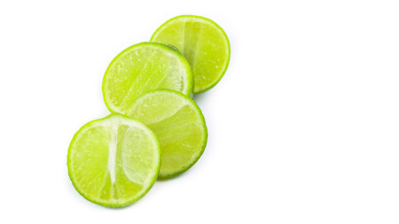 Whole limes and lime halves placed on a white background, highlighting the freshness and vibrant color of the fruit.の写真素材