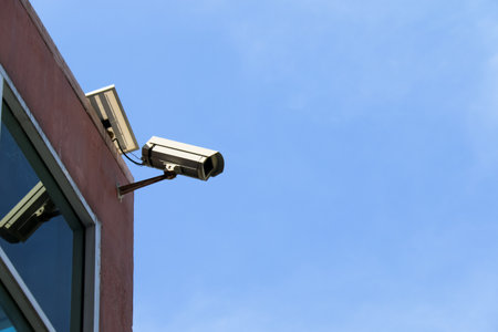 An old yet reliable CCTV camera mounted outdoors, exposed to sun and rain over the years, standing guard to ensure security for homes. A symbol of safety and modern surveillance technology.の写真素材