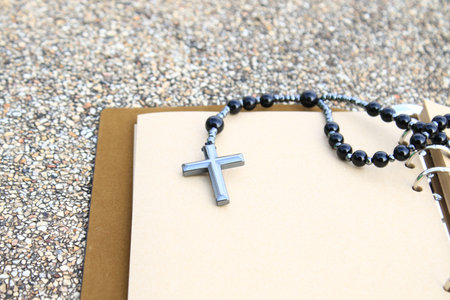 A shiny metal cross rests on an open brown notebook, symbolizing faith, reflection, and devotion....