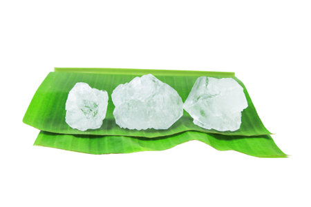 Pieces of alum stone on green banana leaf against white background. Concept of the connection between natural minerals and plant based ingredients in traditional practices and holistic wellness.の写真素材