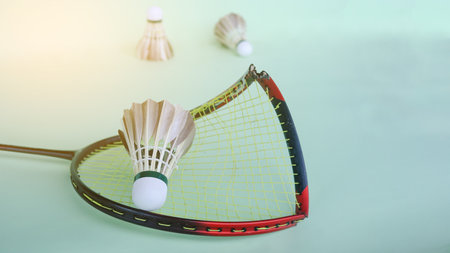 Broken badminton racket with a shuttlecock on a light green surface, endurance and sportsmanship.の写真素材