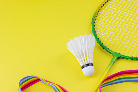 Badminton racket and white shuttlecock, and rainbow ribbon on yellow backgroundの写真素材