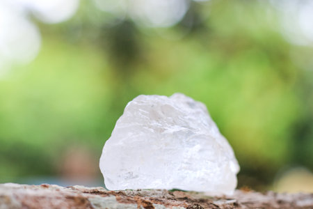 White alum crystal placed on a wooden log with blurred background. Traditional natural remedy in a...