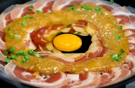 Set of raw marinated sliced pork  with egg yolk preparation for sukiyakiの写真素材