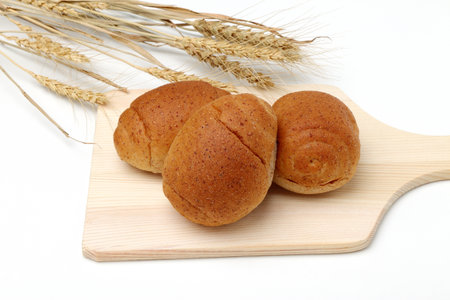 Bread rolls on a cutting board with wheat ears on a white backgroundの写真素材