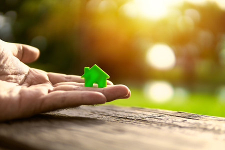 Hand one side carrying a green house model just like giving and sharing..The background is orange sunset.の写真素材