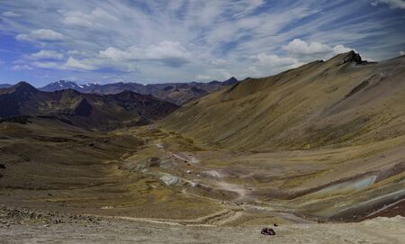 Backside of Apu Ausangate and Rainbow Mountain Peak at Vinicunca Valley. An Andes mountain range with intense red, yellow, orange, green and blue colors. Visitors on the watch point in a hilltopの写真素材