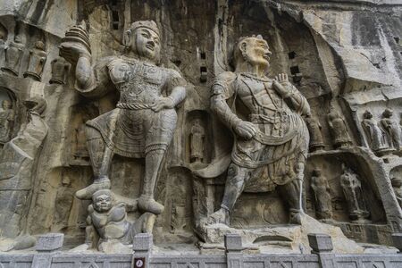 Figure of a mighty guardian and Vajrapani with a thunderbolt holder in Fengxian temple. Longmen Caves in Luoyang, Henan province, Chinaの写真素材