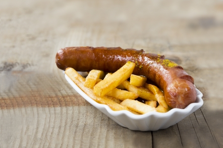 Popular German Fastfood (Saussage with Curry Sauce) Currywurst and French Fries isolated on wooden Tableの写真素材