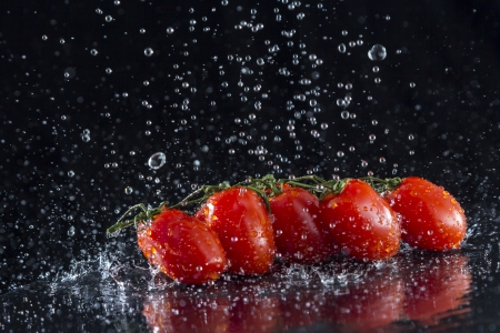 Tomatoes in splashing water on black backgroundの写真素材