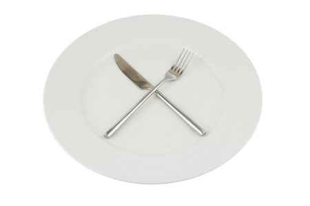 silver knife and fork crossed on a white plate on whiteの写真素材
