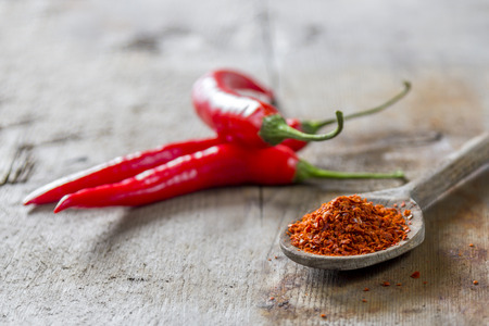 Powdered chilli on a wooden spoon with a red chilli on wooden backgroundの写真素材