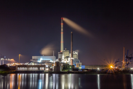power plant at the waterfront with smoking chimney illuminated at nightのeditorial素材